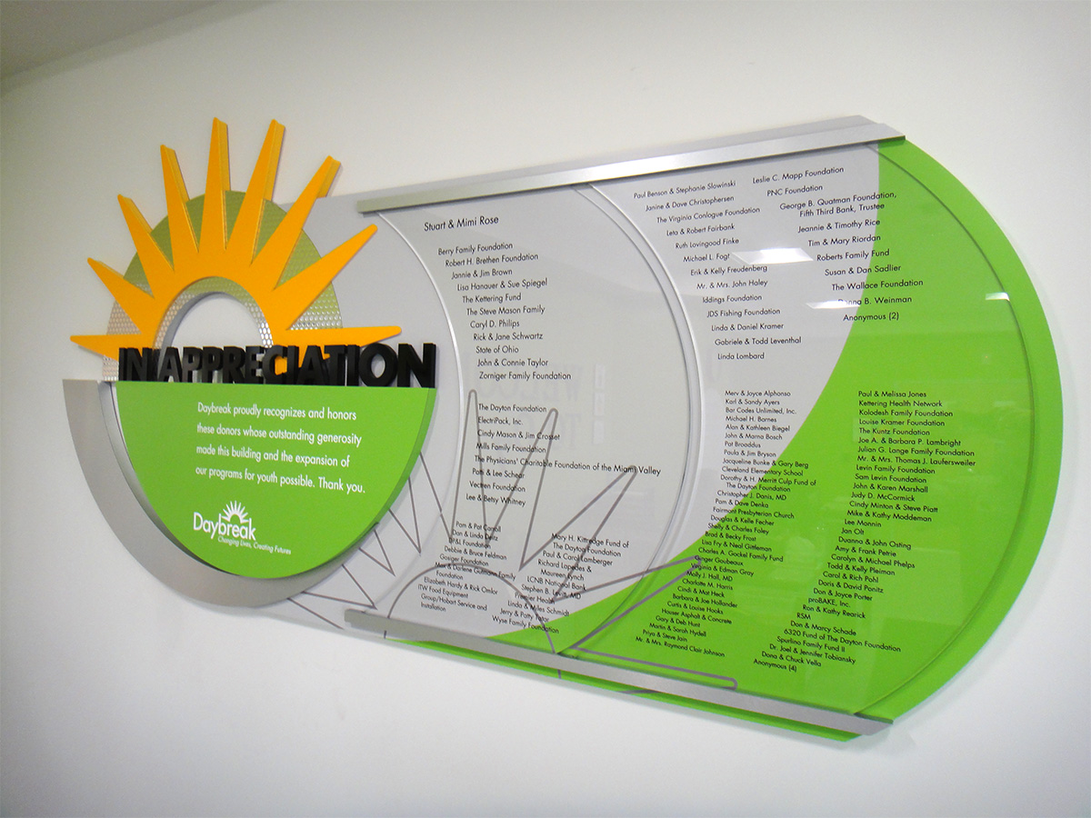 Permanent donor display combining dimensional sun rays, metallic textures, curved acrylic panels, and organized donor listings inspired by the Daybreak logo.
