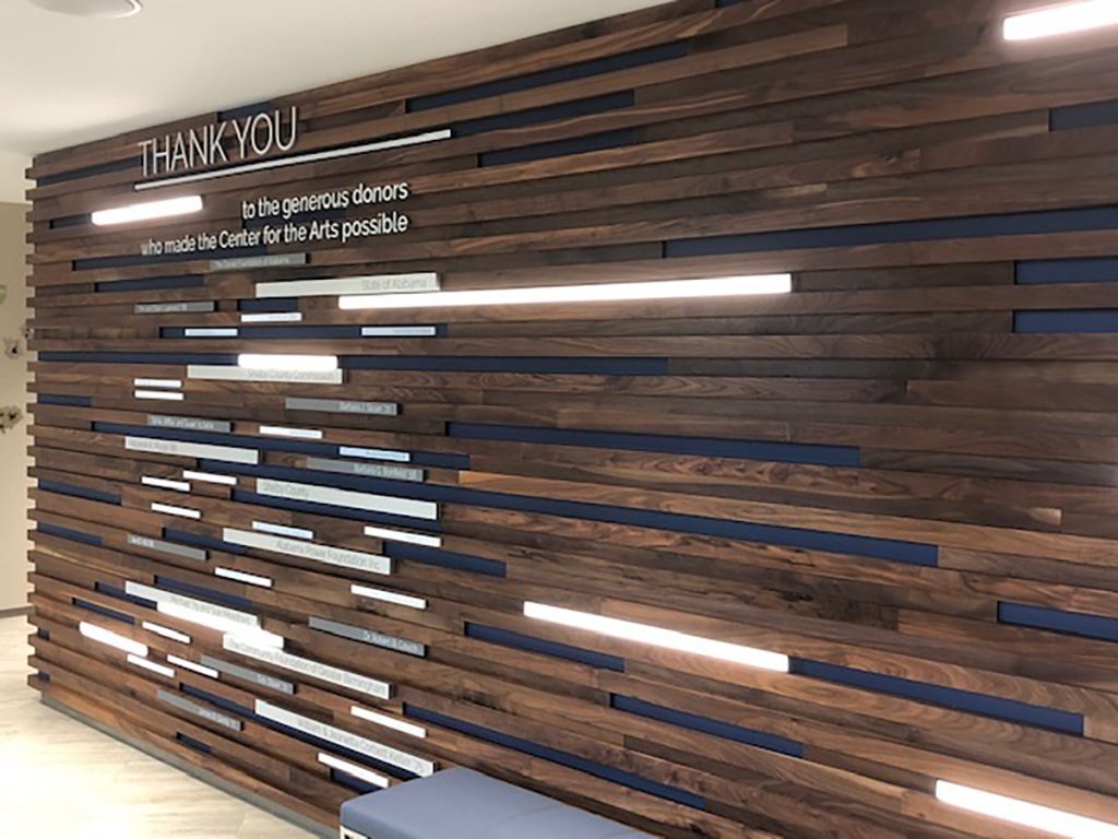 Art center donor recognition display featuring donor nameplates woven throughout a dimensional slatted wood wall using the Add-On System.