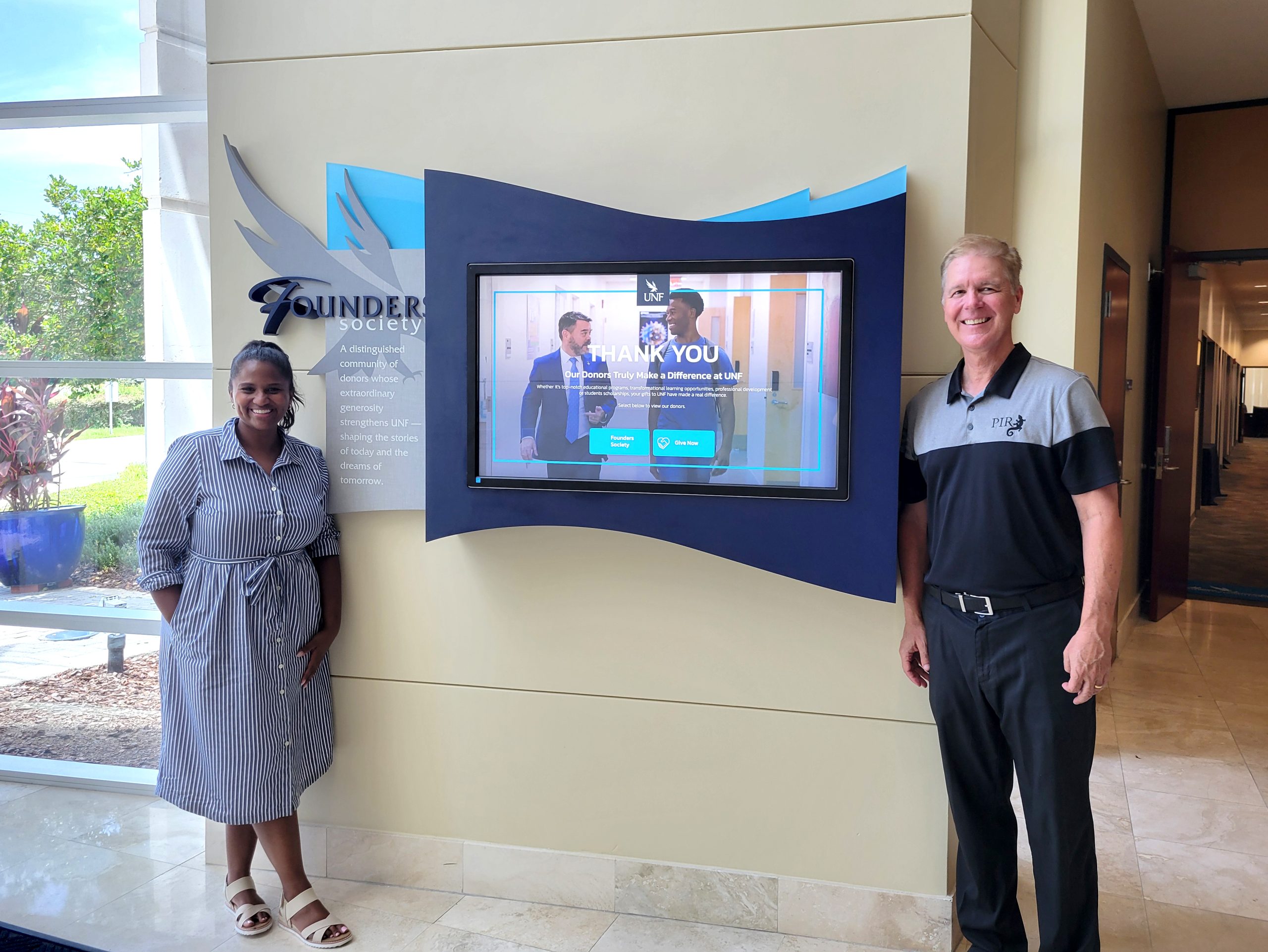 PIR team members standing beside the University of North Florida Founders Society interactive donor recognition display.
