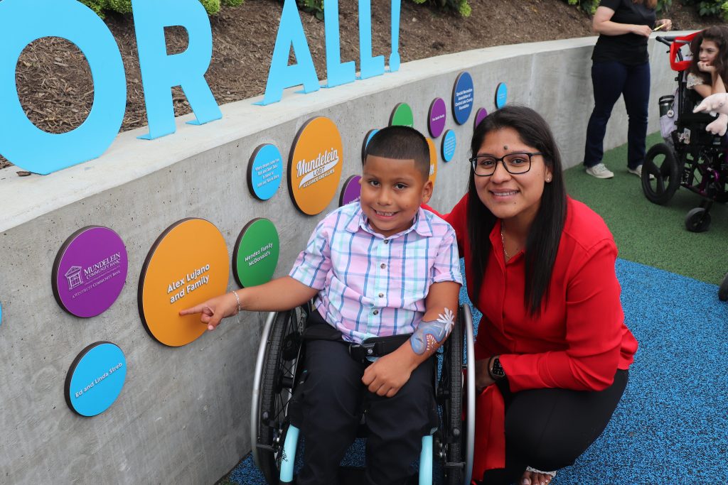 Boy in wheelchair and his mother point to a donor plate displaying their name.