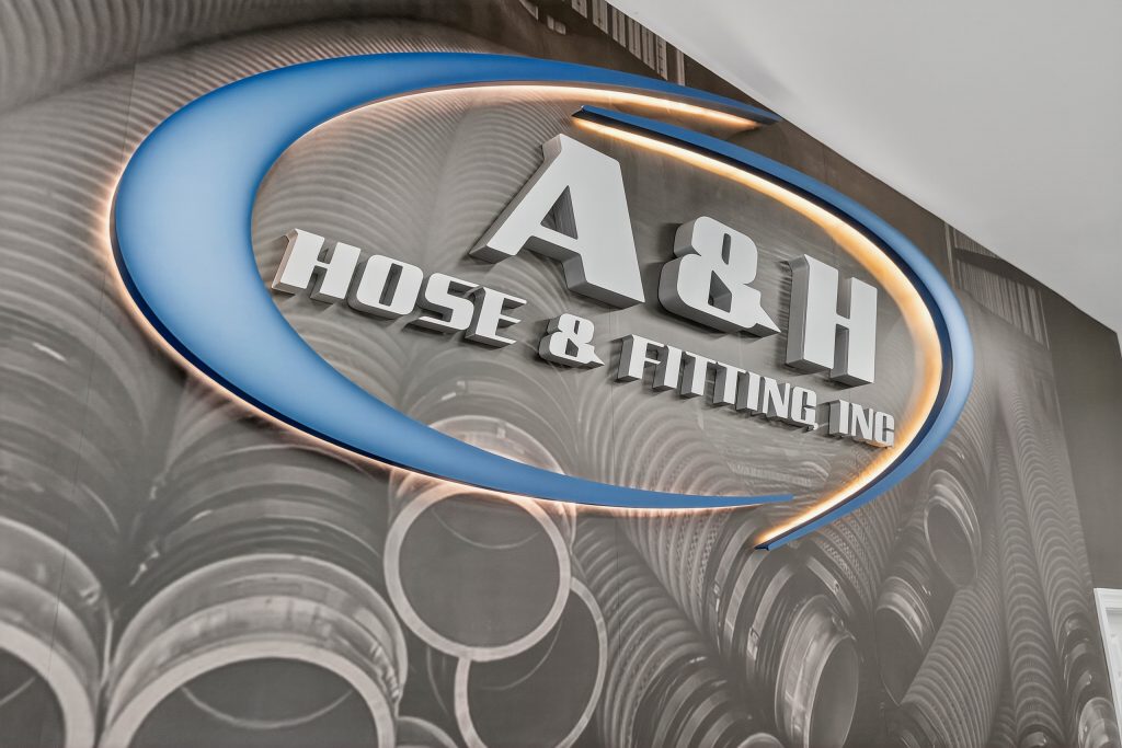A close up photo of A & H Hose's lobby signage that features edge lit freestanding letters. Custom wallpaper is also placed behind featuring a black and white photo of hoses.