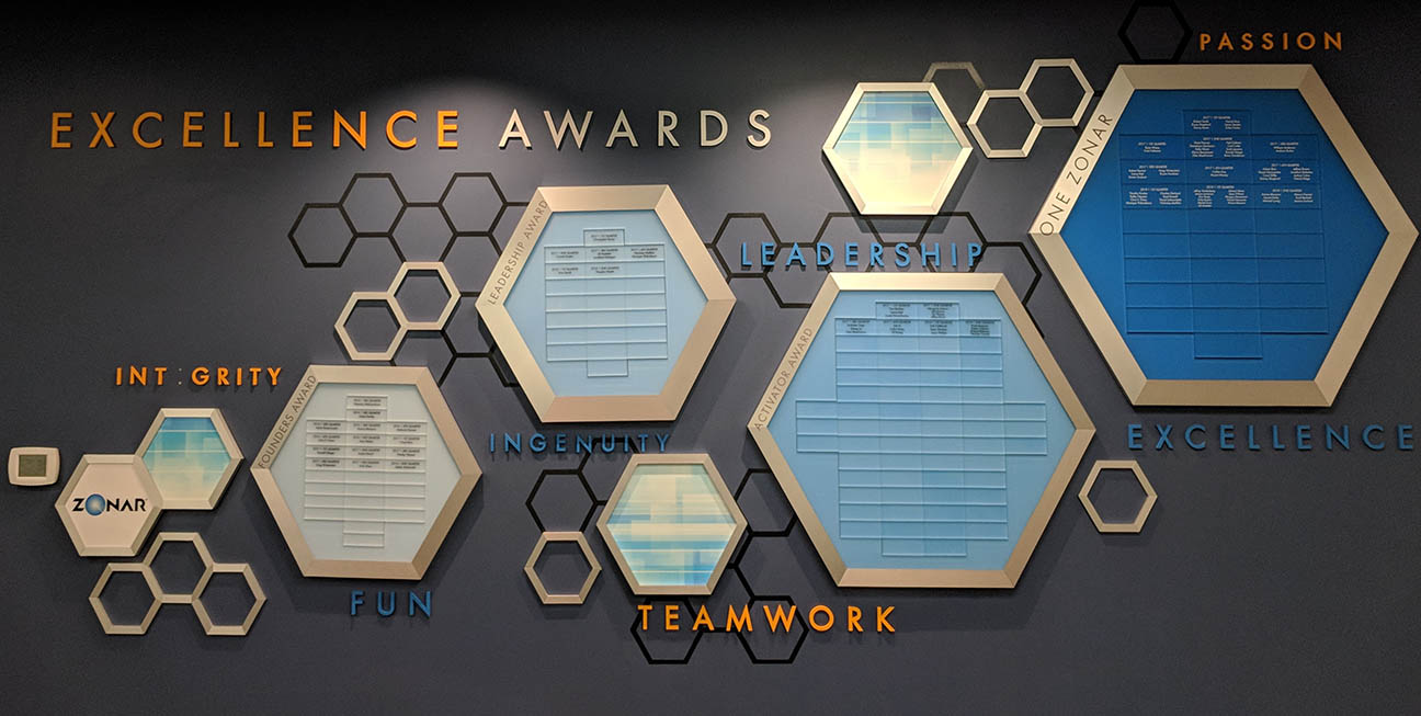 Hexagon-themed employee recognition wall at Zonar Systems displaying Excellence Awards with addable name plates for quarterly winners across multiple award categories.