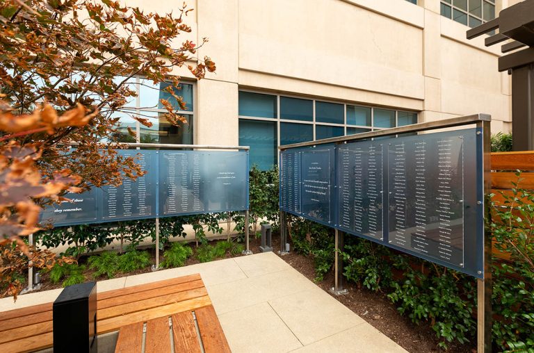 Outdoor memorial display at Hoag Hospital featuring blue-tinted panels with memorial names in a landscaped garden setting