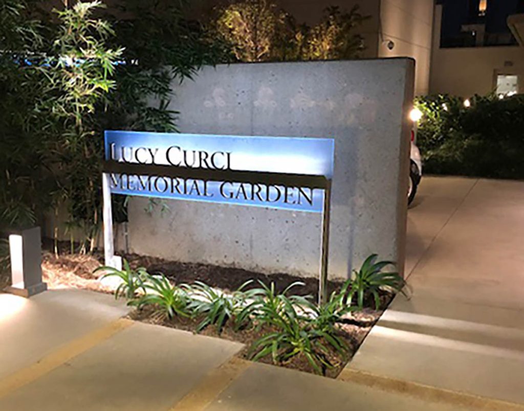 Illuminated Lucy Curci Memorial Garden sign at Hoag Hospital with soft lighting and landscaped surroundings at night