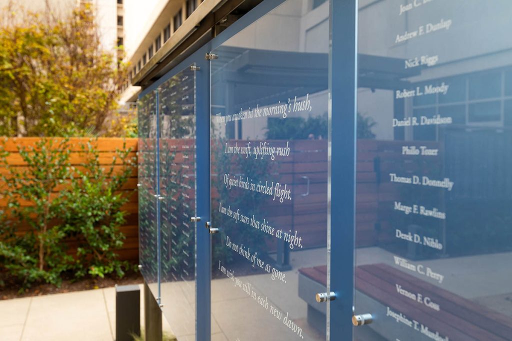 Close-up of outdoor memorial display panels with names and printed quote on blue-tinted 3-Form at Hoag Hospital