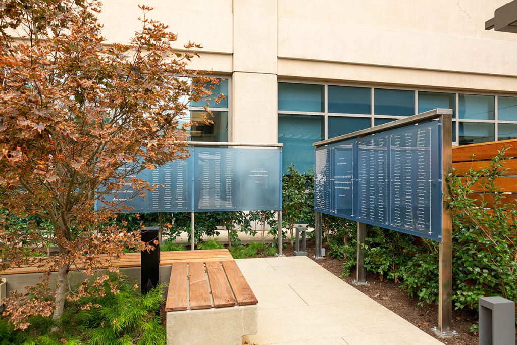 Outdoor memorial display with blue panels and bench in landscaped hospital garden at Hoag Hospital