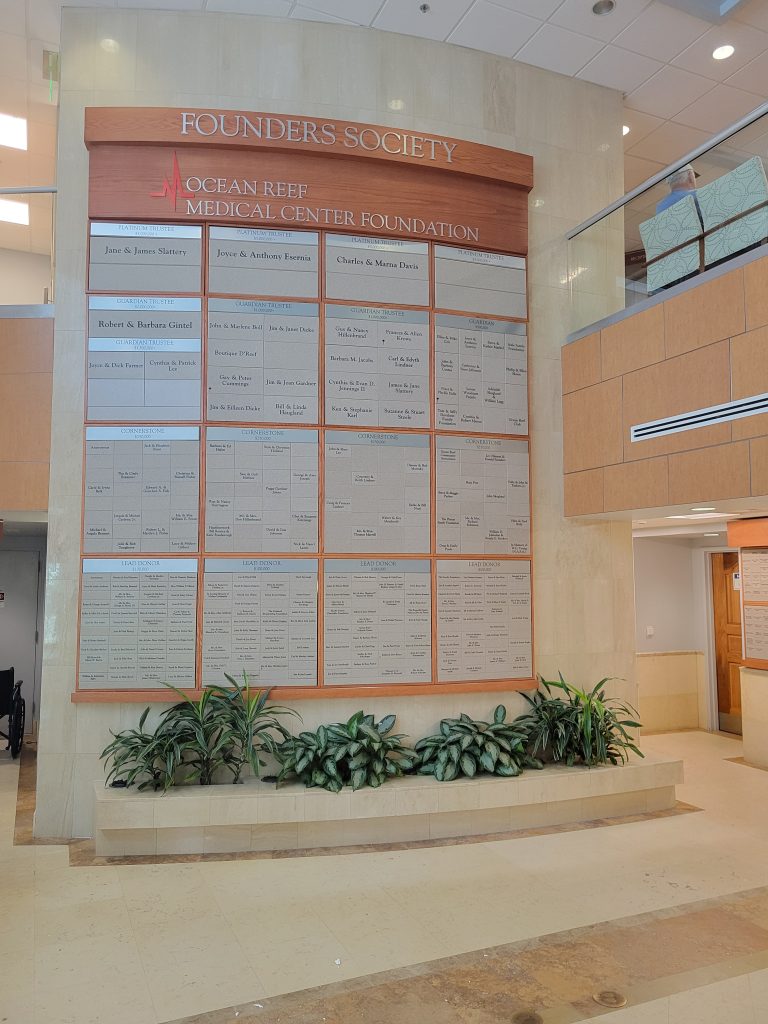 Completed donor recognition display expansion at Ocean Reef Medical Center featuring a custom wood donor wall with expanded giving categories and Corian® donor nameplates.