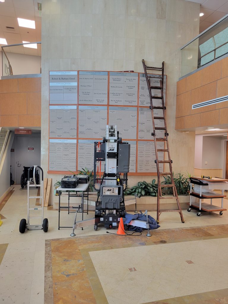 Installation of a donor recognition display expansion at Ocean Reef Medical Center using lift equipment to modify an existing donor wall.