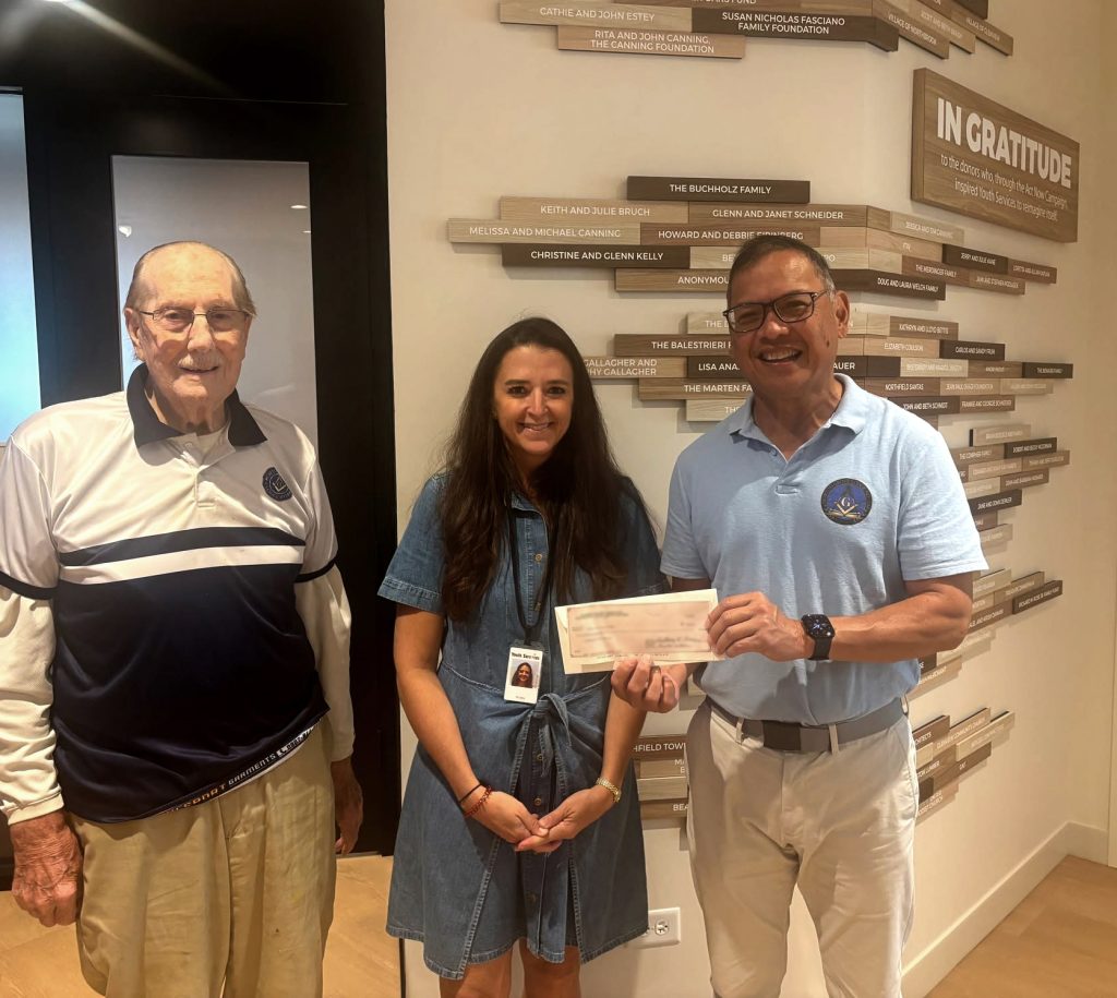 Donors giving a check for additional funding in front of a donor display for a capital campaign.