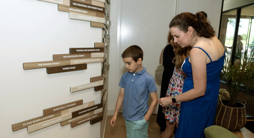 Donors looking for their names on the modular, nonprofit donor recognition display for the youth services center.