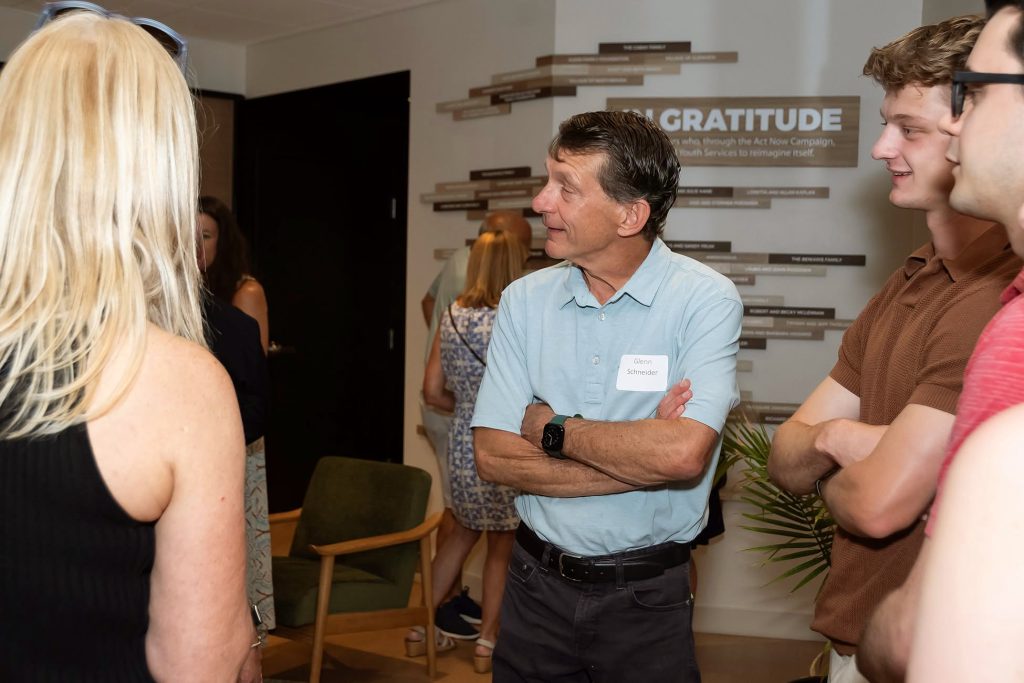 Donors converse while standing in front of a donor display for their Youth Services capital campaign during a grand opening event.