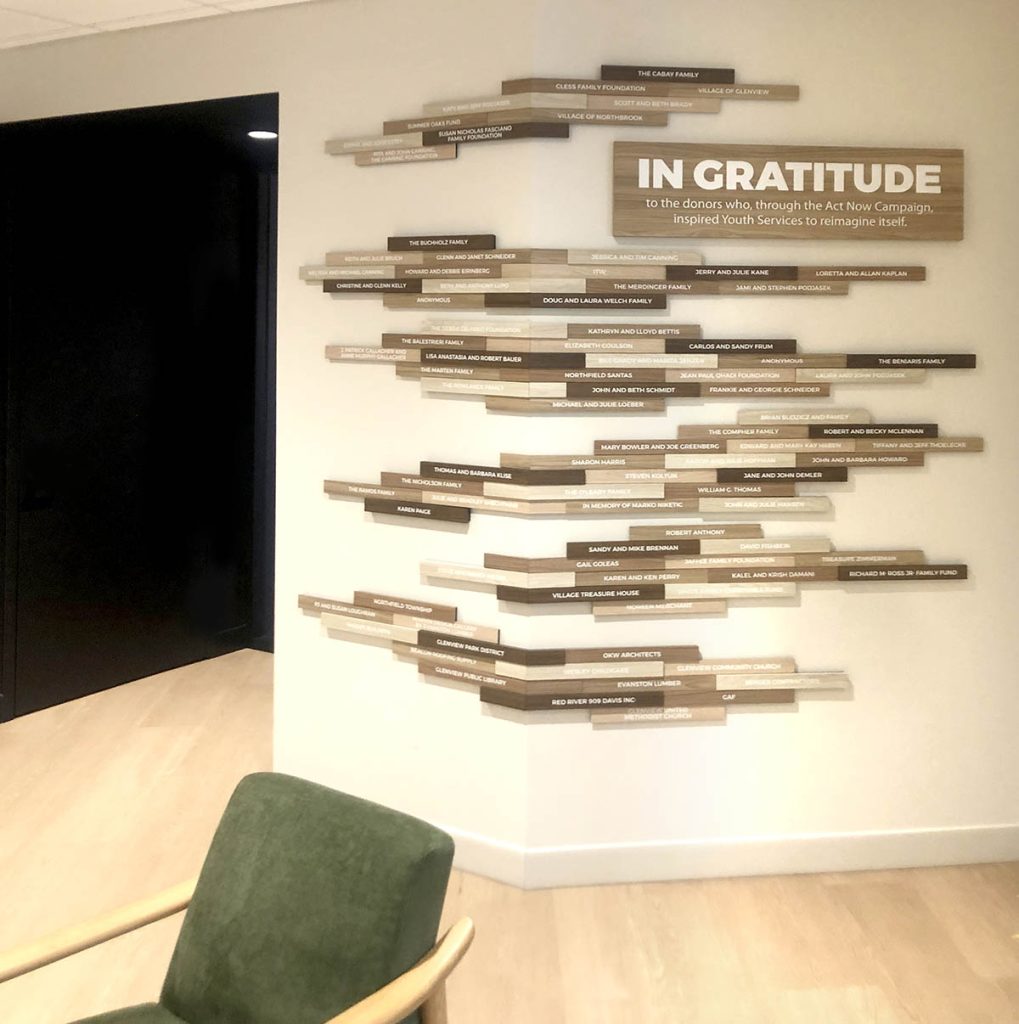 Youth Services nonprofit donor recognition display featuring staggered wood-tone nameplates in varying sizes and an “In Gratitude” recognition panel.